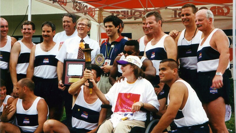 Runners from the Law Enforcement Torch Run together in a group, a young woman in a wheel chair is holding the Eternal Flame. 