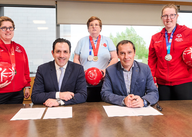 SOEE and TME representatives signing the agreement while Special Olympics athletes hold footballs