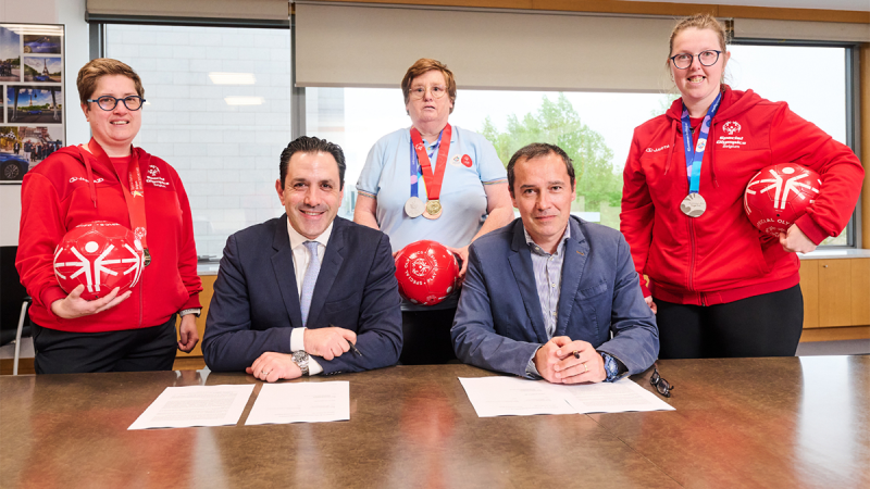 SOEE and TME representatives signing the agreement while Special Olympics athletes hold footballs