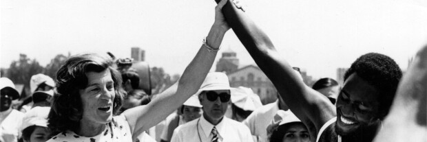 Eunice Kennedy Shriver holding an athletes arm up in victory. 