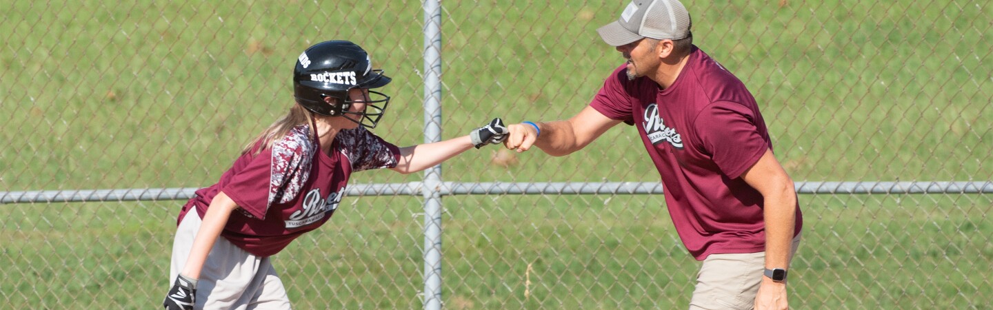 Female baseball player fist-bumping a coach. 