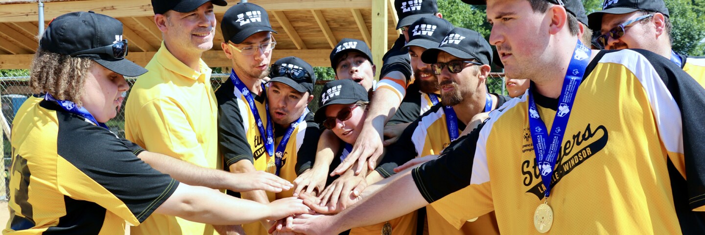 Athletes standing in a semi-circle with all hands touching in the center. 