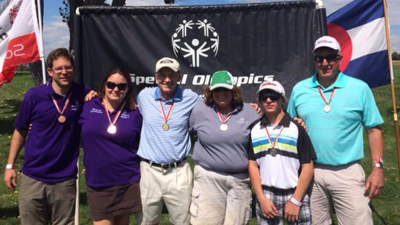 A group of six Special Olympics athletes and Unified partners pose for a photo in front of a banner that says Special Olympics. 