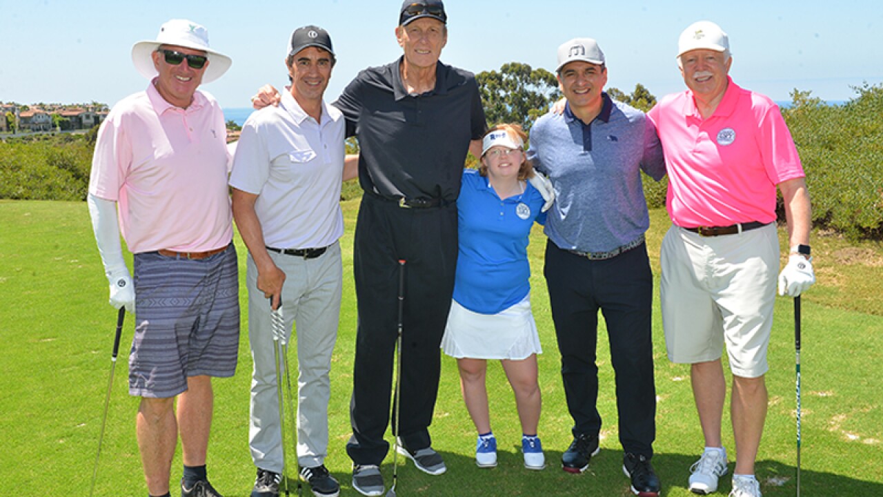 Amy standing side by side in a group with Rick Barry and celebrity golfers.