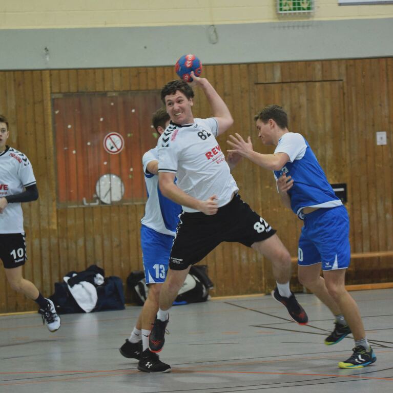 Player prepares to throw the ball while two players from the opposing team attempt to block. 