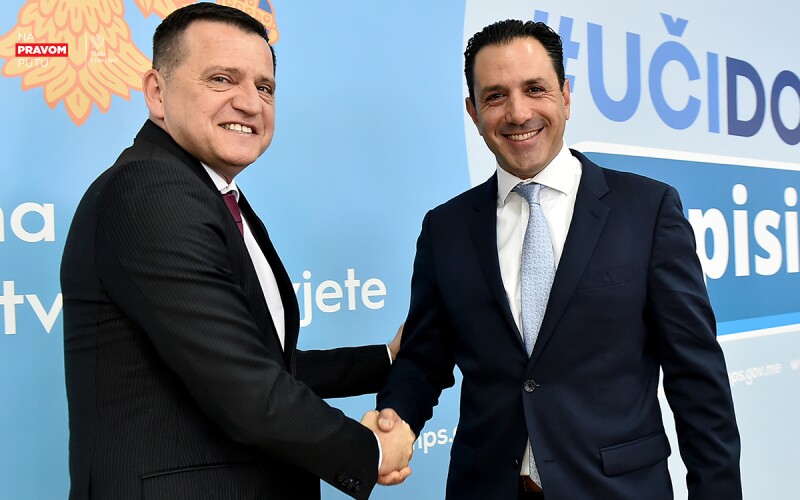 Two men wearing suits, shake hands and smile at the camera