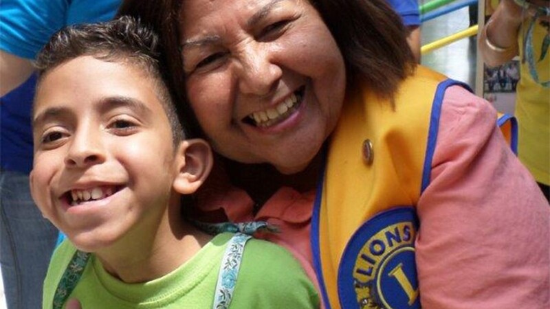 A woman in a yellow Lions Clubs vest hugging a young boy and both are smiling. 