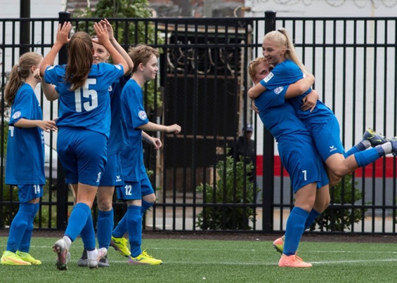 Group of girls wearing a blue uniform celebrating on a football field.