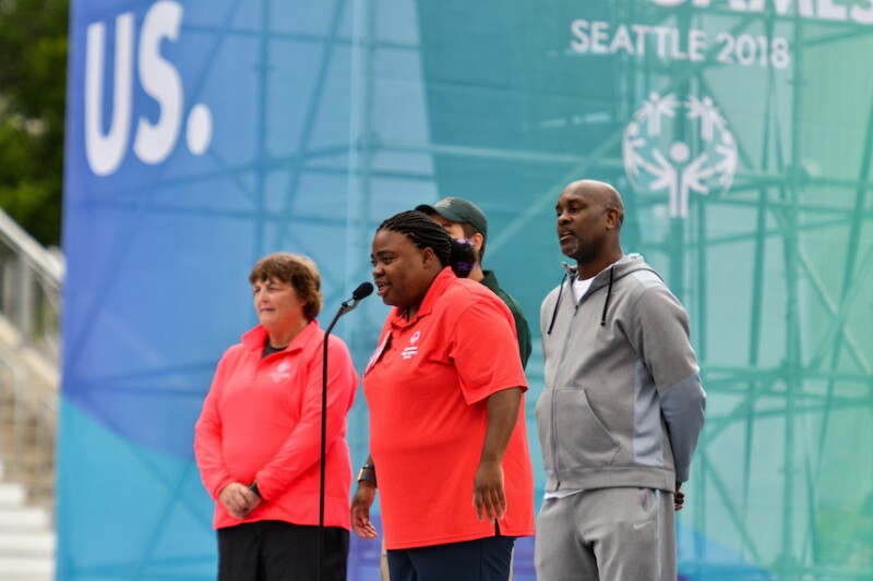 A Special Olympics athlete stands on a stage and speaks into a microphone. 