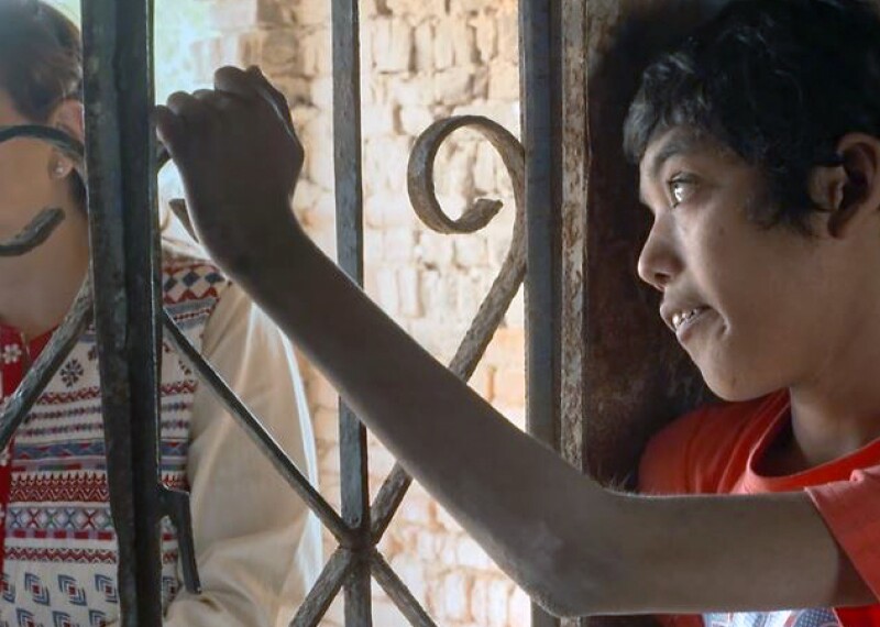 Young man holding onto a decorative iron bar and looking off into the distance. 