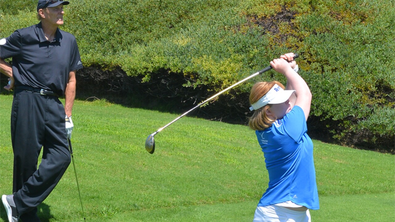 Amy has swung at a ball on the green as NBA Hall of Famer Rick Berry watches. 