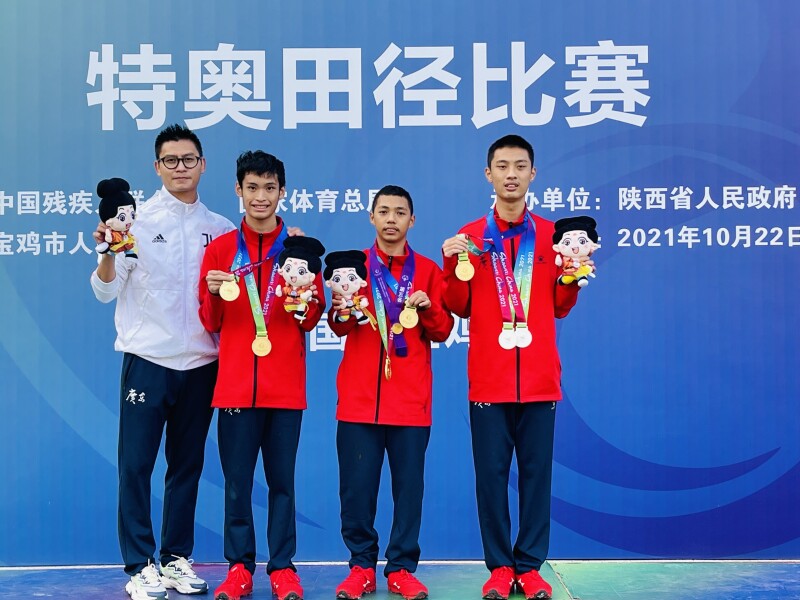 Coach Peng Shaojian standing with three athletes showing off their medals. 