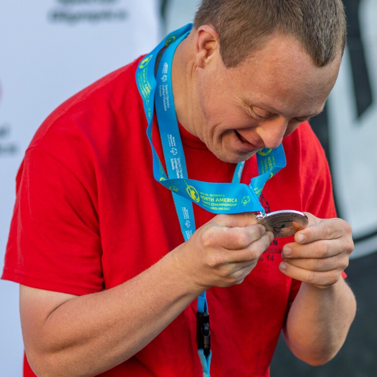 Male athlete looking at his medal he's holding and smiling. 