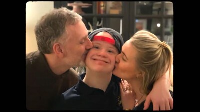 Mother and father kissing their son on the cheeks. 