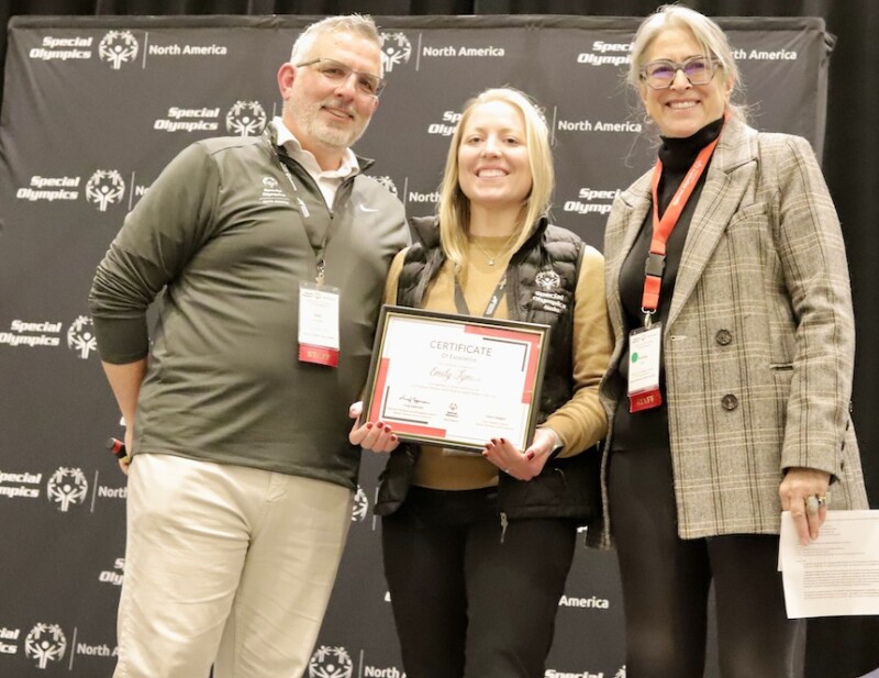 Three individuals pose for a photo. The middle person is holding a certificate. 