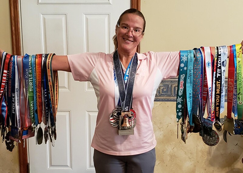 Amber is standing showing off all of her medals she has earned from the virtual events. 