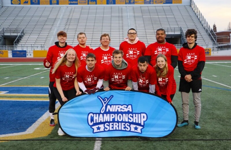 The University of Nebraska Lincoln Unified Flag Football team stands on the football field. They wear read shirts and stand behind a sign that says "NIRSA Championship Series". 