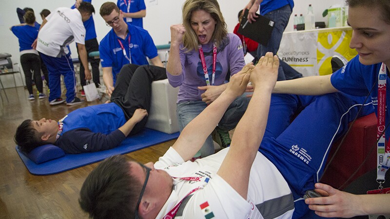 An athlete performing crunches while volunteer and Julian Micheles cheers him on. 