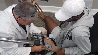 Dionte Foster sitting in a char on the right getting fitted with his athletic prosthetic. 