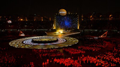 Wide shot the opening ceremony stage. Athlete spectators are lit up with a read spotlight.