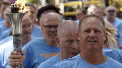 A man in a Final Leg blue t-shirt holds a lit torch with several other men lined up behind him.