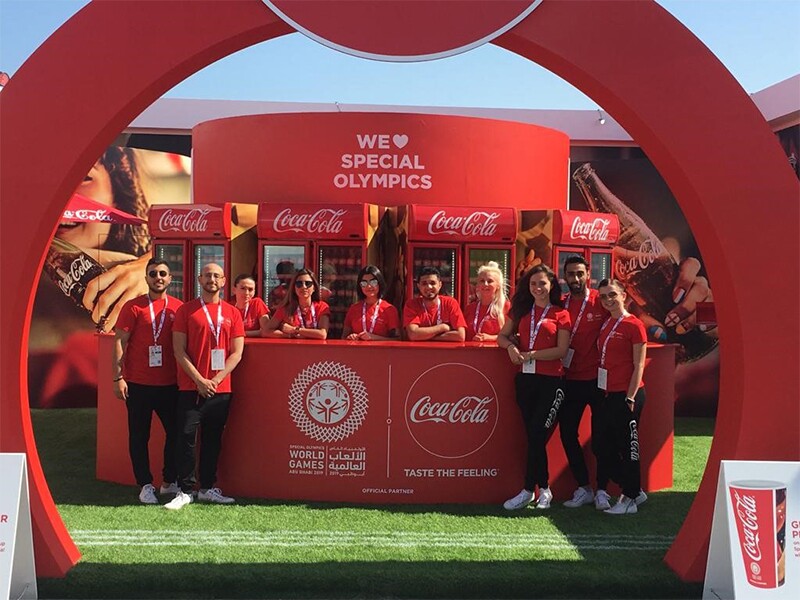 Coca Cola representatives standing at the Coca Cola booth in Abu Dhabi at the summer games. 