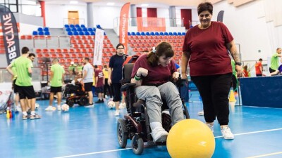 Woman in wheelchair kicking a big yellow ball. 