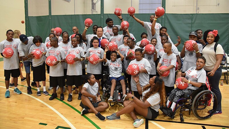 Sam Perkins along with a group of athletes hold red Play Unified balls in a gymnasium posing for a group photo. 