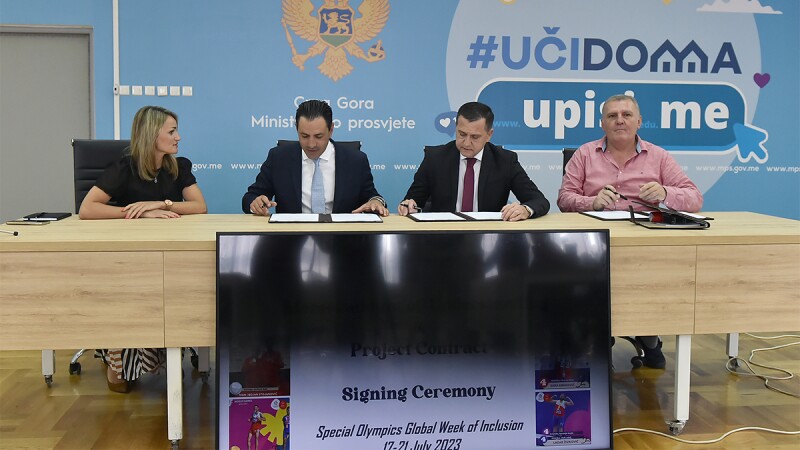 Four people, one female and three male, sitting at a table, with the two male in the middle signing papers