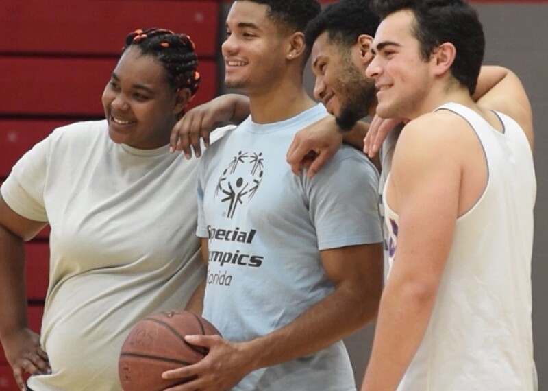 Group of four with their arms on one another shoulders; one is holding a basketball. 