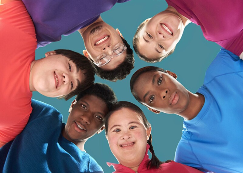 Six people standing in a circle with their arms around one another looking down as the photographer is looking up taking a photo of them. 