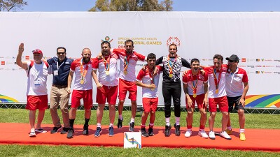 Young men dressed in red and white football kits and wearing gold medals line up with arms around each other smiling in front of promotional poster for Special Olympics Malta Invitational Games 2022. 