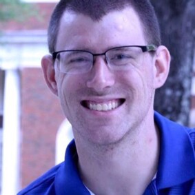 RJ smiling for a photo; he has on glasses and a blue polo. 