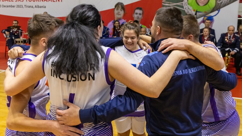 Bosnian team gathers on basketball court to celebrate and a female team member smiles