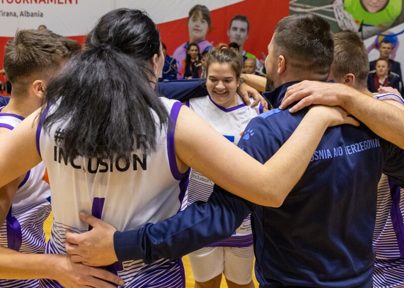 Bosnian team gathers on basketball court to celebrate and a female team member smiles