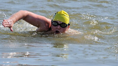 Athlete in a yellow swim cap focuses on his strokes.  