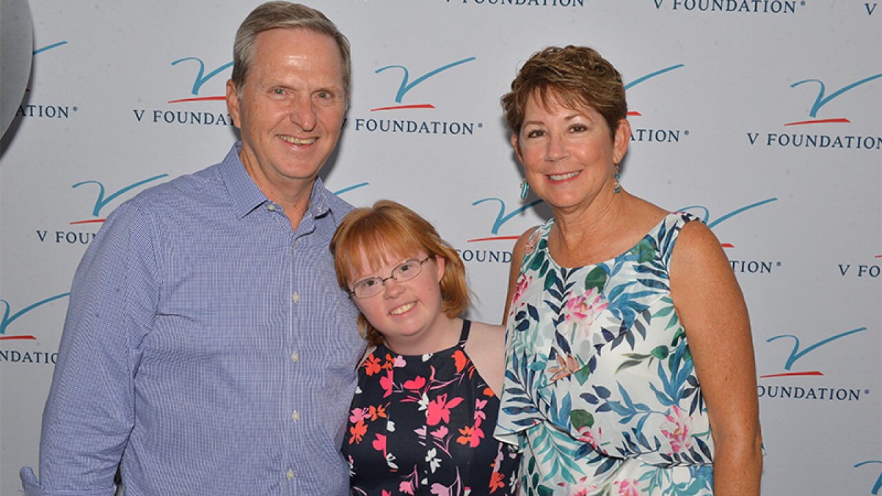 Amy's parents stand on either side of her in front of signage that reads, V Foundation.