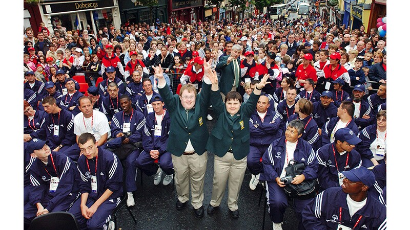 Two athletes standing with their arms up in the air and they are surrounded by other athletes. 