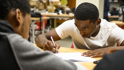 A teenage student writing on a sheet of paper.