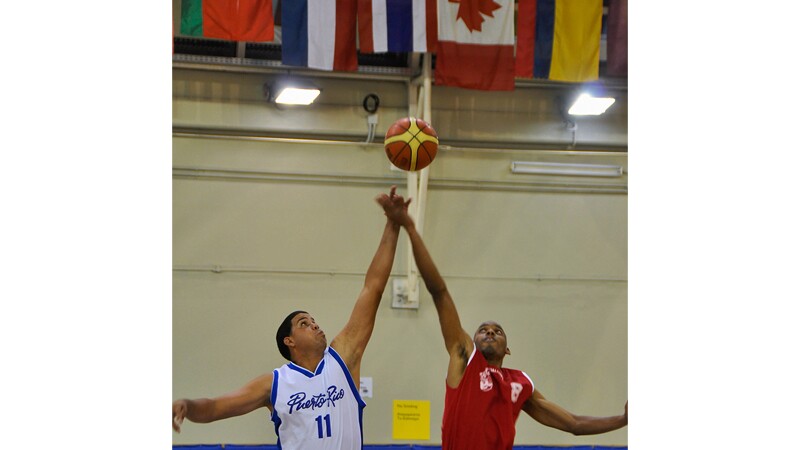 Two athletes from opposing teams jumping for the basketball. 