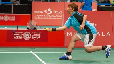 Special Olympics athlete running for the birdie with badminton racquet.