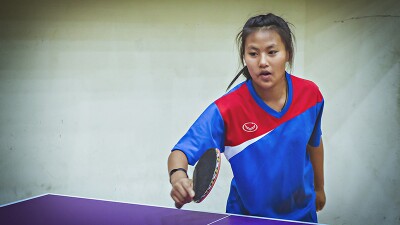 Chutipa in a blue, red, and white team shirt playing table tennis.