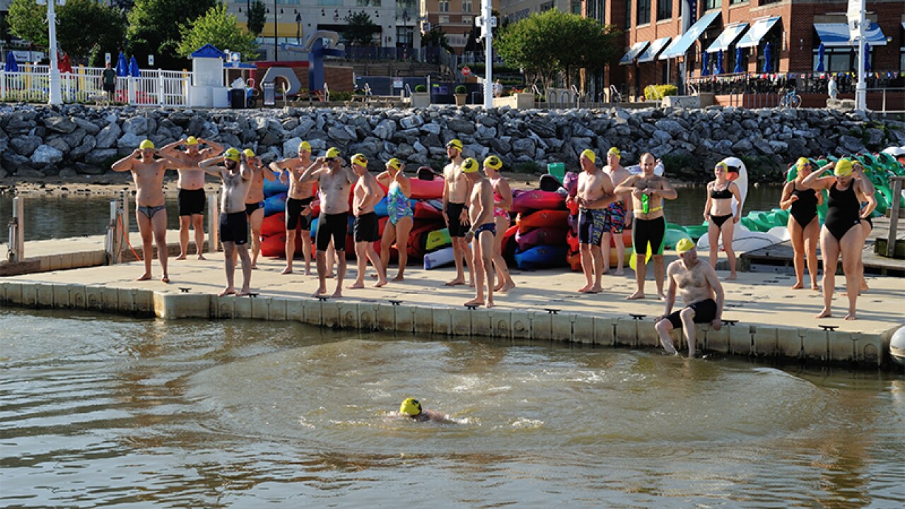 Swimmers standing on the dock preparing to swim, one athlete is already in the water and another is sitting with his feet in the water. 