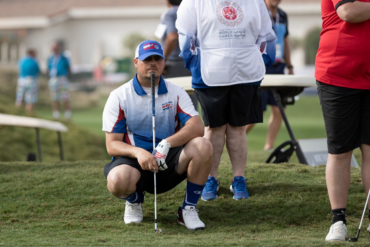 Golfer crouching down on the green looking off into the distance.