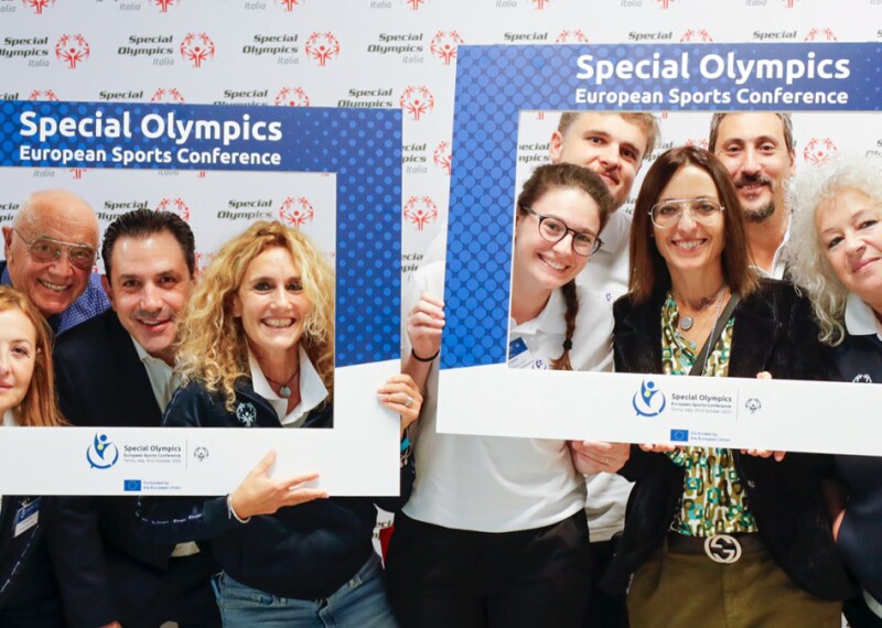 Attendants to the SOEE Sports Conference smiling at the camera while holding branded signs