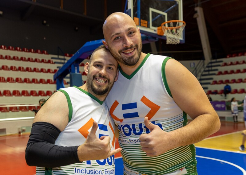 Two men wearing basketball jerseys smile while posing for the camera