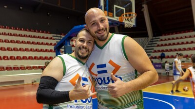 Two men wearing basketball jerseys smile while posing for the camera