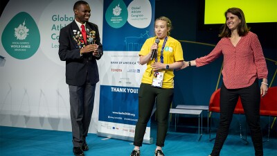 A young man walking toward a young woman that is speaking on stage. 