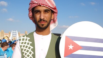 Volunteer at the Special Olympics World Game Abu Dhabi 2019 wears a volunteer vest and holds a sign with a picture of the Cuban flag.