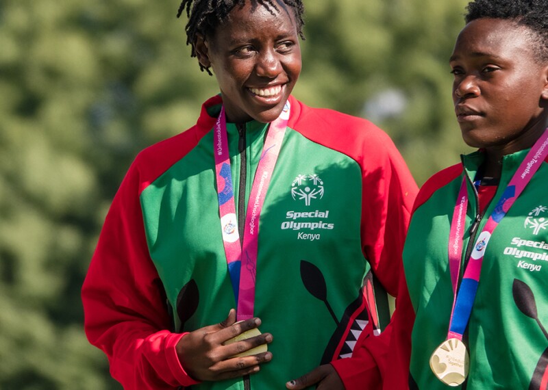 athlete smiling holding medal next to teammate 